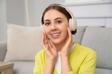 Evde diş teli takan kulaklıklı genç bir kadın var.