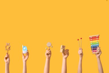 Sarı arka planda bebek aksesuarları tutan eller.