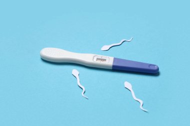 Mavi arka planda sperm hücreleri ve hamilelik testi