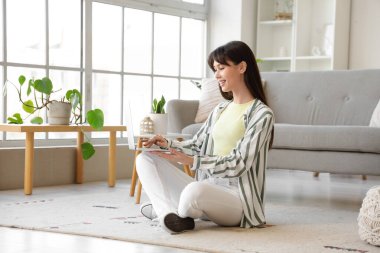 Evde dizüstü bilgisayar kullanan genç bir kadın.