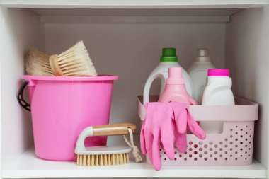 Mutfakta farklı temizlik malzemeleri, fırçalar ve pembe lastik eldivenlerle dolu bir sepet aç.