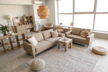 Rahat gri koltukları, kahve masası, ev bitkileri ve büyük pencereli şık bir oturma odası.