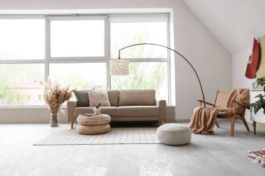 Şık oturma odasının içinde rahat gri kanepe, puf ve otlar var.