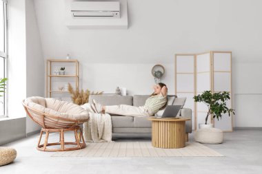 Güzel, genç bir kadın şık bir oturma odasında, rahat, gri bir kanepede yatıyor.