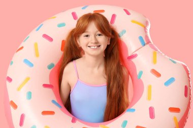 Pembe arka planda şişme yüzük takan kızıl saçlı küçük kız.