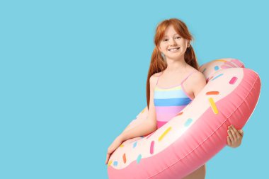 Mavi arka planda şişme yüzüğü olan kızıl saçlı küçük kız.