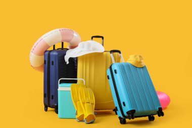 Sarı arka planda plaj aksesuarları olan bavullar.