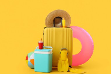 Sarı arka planda plaj aksesuarlarıyla dolu bavul.