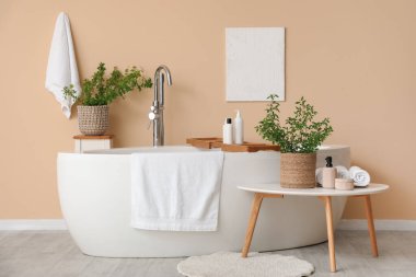 Küveti, kozmetik ürünleri, havluları ve masa üstünde vazolar içinde çiçek açan yeşil dalları olan şık bir banyo.