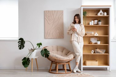 Evdeki kozanın yanında cep telefonu kullanan genç bir kadın.