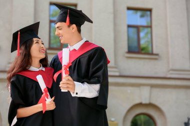 Üniversitenin yakınında, diplomalı, mutlu bir çift mezun öğrenci.