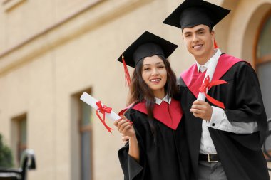 Üniversitenin yakınında, diplomalı, mutlu bir çift mezun öğrenci.