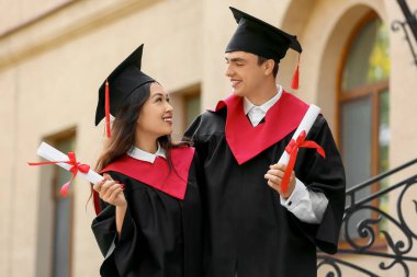 Üniversitenin yakınında, diplomalı, mutlu bir çift mezun öğrenci.