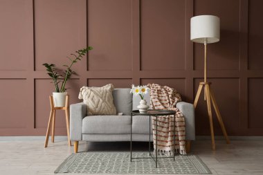 İçinde kanepe, lamba ve vazoda papatya olan oturma odası.