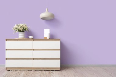 Papatya çayı vazosu ve oda odasındaki leylak duvarın yanındaki çekmecelerin üzerinde kahve fincanı.