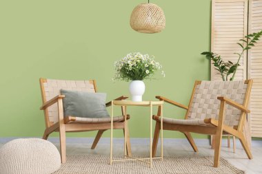 Oturma odasının içinde koltuklar, masa ve papatyalar vazoda.