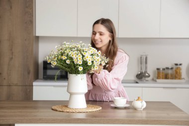 Mutfaktaki masada papatyaları olan genç bir kadın ve vazo.