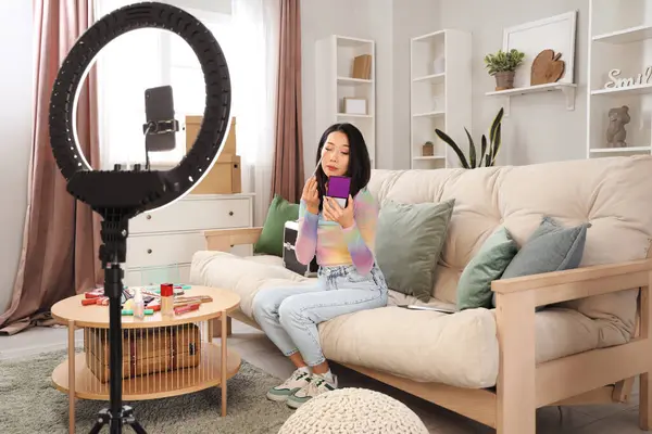 Kadın Asyalı güzellik blogcusu evde video kaydederken göz farı uyguluyor