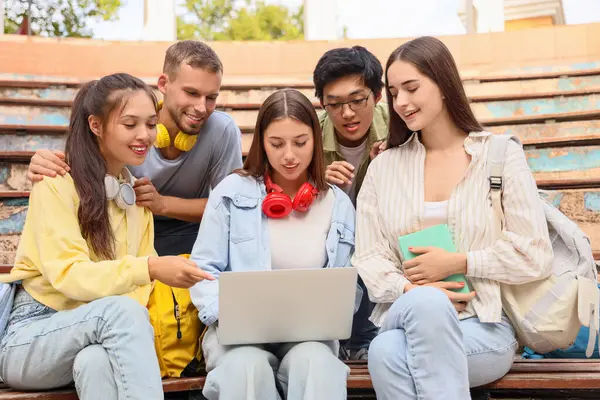 Dışarıdaki banklarda dizüstü bilgisayarla çalışan bir grup öğrenci.