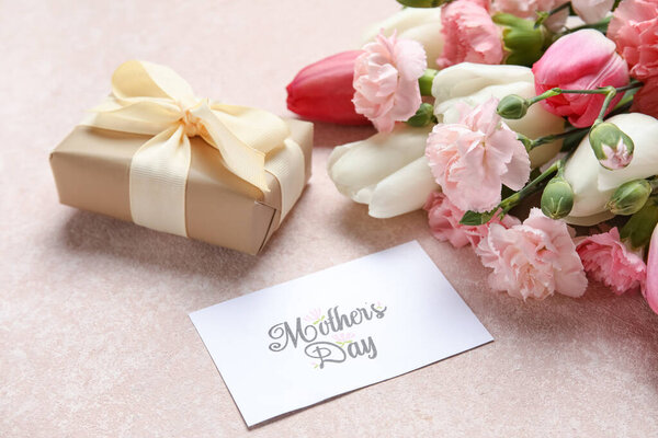 Букет различных красивых цветов с поздравительной открыткой и подарочной коробкой на бежевом фоне, крупным планом. Праздник Дня матери