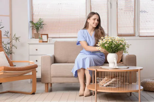 Oturma odasındaki masada papatyaları olan genç bir kadın ve vazo.
