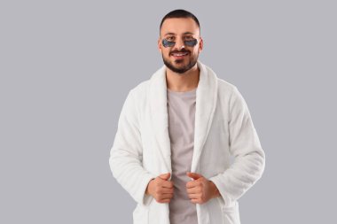 Gri arka planda göz bantları olan bornozlu genç bir adam.