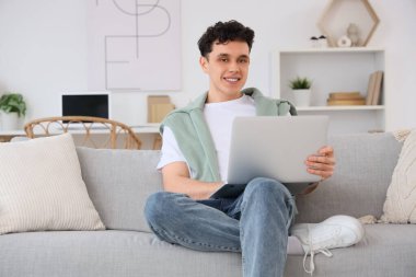 Evdeki kanepede dizüstü bilgisayarla çalışan genç adam.