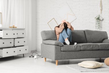 Deprem sırasında oturma odasında başını koltuğa koyan korkmuş genç bir kadın.