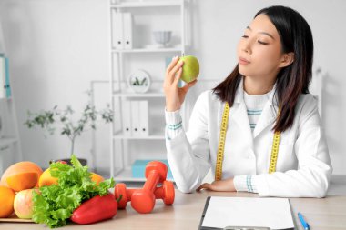 Ofisinde elma bulunan Asyalı kadın beslenme uzmanı.