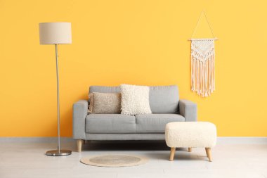 Turuncu duvarın yanında lamba ve divanı olan rahat gri kanepe.