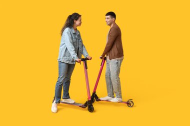 Sarı arka planda modern elektrikli scooter kullanan güzel genç bir çift.