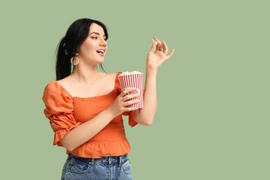 Yeşil arka planda patlamış mısır kovası olan mutlu genç bir kadın.