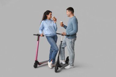 Modern elektrikli scooterları ve gri arka planda kağıt kahve fincanları olan güzel bir çift.
