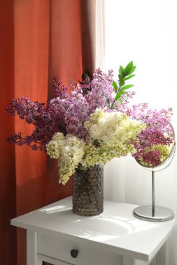 Pencerenin yanındaki masada çiçek açan bir vazo.