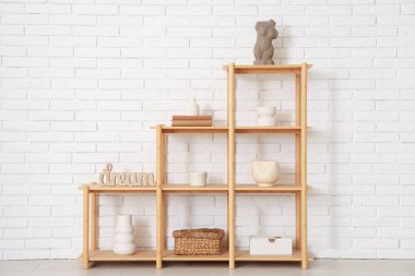 Beyaz tuğla duvarın yanında kitap ve dekor bulunan ahşap raf ünitesi.
