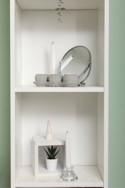 Oturma odasının içinde küçük yuvarlak aynalı, mumlu ve dekorlu raf ünitesi, yakın plan.