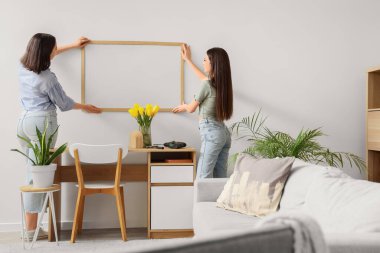 Evdeki ışık duvarında boş bir çerçeve asılı genç kadınlar, arka manzara