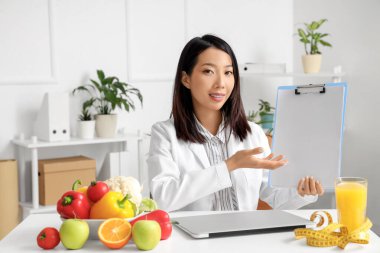 Ofisinde panosu olan Asyalı kadın beslenme uzmanı.