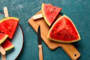 Ahşap tahta ve tabakta yeşil arka planda tatlı karpuz çubukları var.