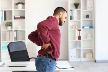 Ofiste sırt ağrısı çeken genç bir adam.