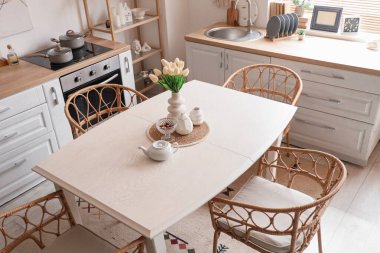 Ahşap yemek masası, rattan koltuklar ve şık mutfağın içindeki beyaz tezgahlar.