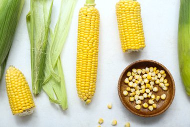 Taze mısır koçanları ve beyaz masada çekirdekleri olan ahşap kase.