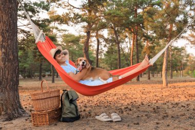 Beagle köpeği olan genç adam dışarıda kırmızı bir hamakta yatıyor.