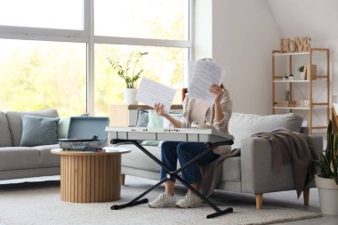 Not kağıtları ve sentezleyicisiyle evdeki kanepede oturan kadın sanatçı.