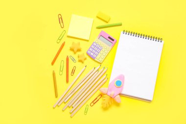 Plastikten yapılmış roket ve sarı zemin üzerinde kırtasiye malzemesi olan boş bir defter.