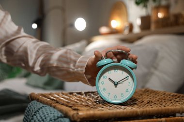 Geceleri yatak odasındaki hasır masanın alarmını kapatan genç bir kadın.