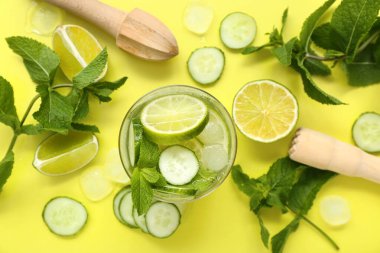 Bir bardak salatalıklı mojito ve sarı arka planda meyve sıkacağı.