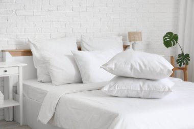 Beyaz battaniyeli rahat yatak ve şık yatak odasında yumuşak yastıklar, yakın çekim.