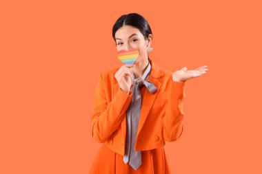 Turuncu arka planda gökkuşağı kalpli güzel bir genç kadın. LGBT kavramı