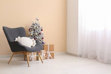 Koltuk ve Noel ağacı. Odada bej duvarın yanında hediye kutuları var.